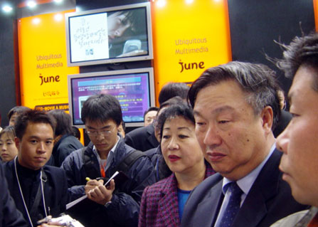 Wang Xudong (on right), Minister of the Information Industry, is shown in the SK Telecom booth watching the demonstration of June, a 3rd generation multimedia and satellite digital mobile broadcasting service.